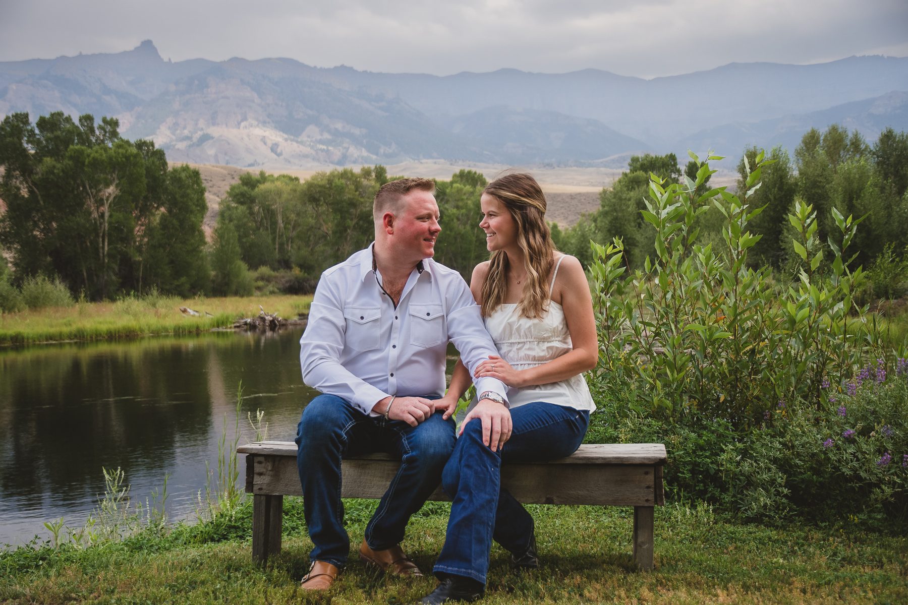 Mariah and Gabe on a bench by the river with mountains behind