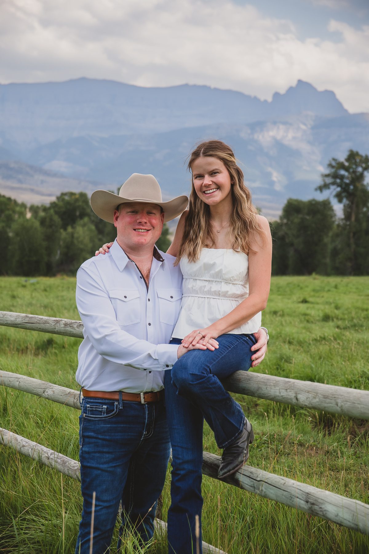 Mariah and Gabe on a ranch fence with mountains behind